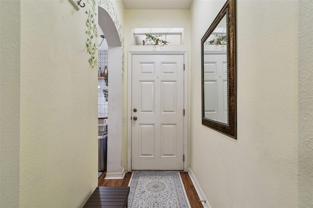 doorway to outside featuring dark wood-style floors, arched walkways, and baseboards