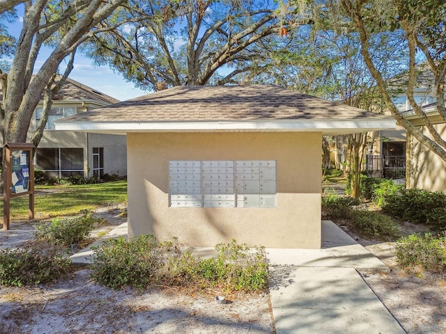 exterior space featuring a shingled roof, mail area, and stucco siding