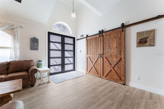 entryway with high vaulted ceiling, ornamental molding, a barn door, and light hardwood / wood-style floors