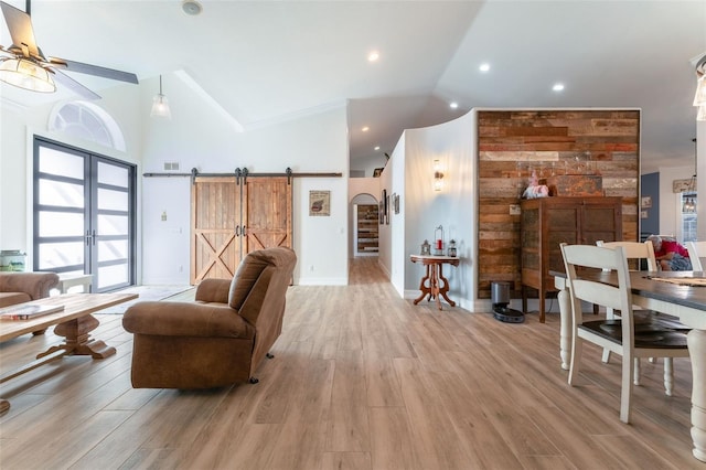 living room with light hardwood / wood-style flooring, ceiling fan, high vaulted ceiling, a barn door, and french doors