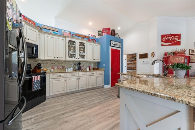 kitchen featuring vaulted ceiling, black appliances, sink, light hardwood / wood-style floors, and light stone counters