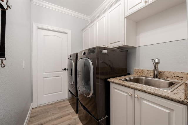 laundry area featuring washing machine and clothes dryer, sink, cabinets, light wood-type flooring, and ornamental molding