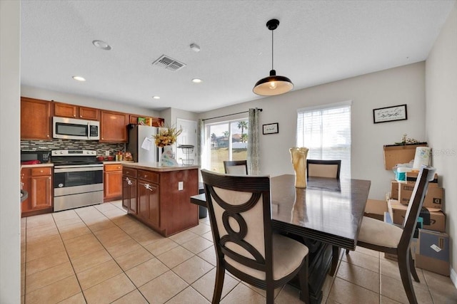 kitchen with a center island, appliances with stainless steel finishes, light tile patterned flooring, decorative backsplash, and pendant lighting