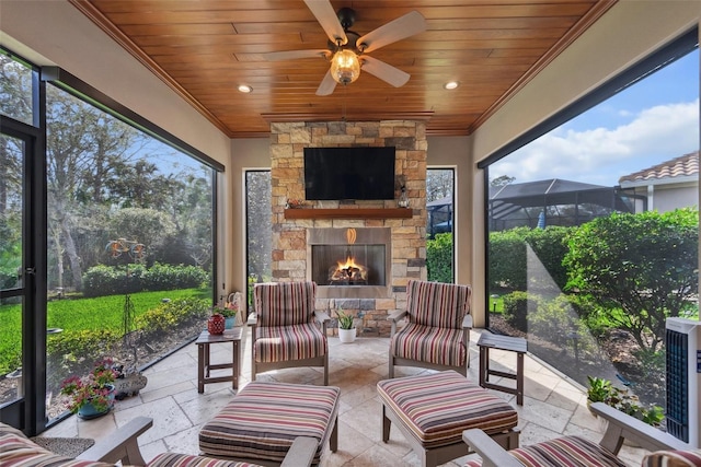 sunroom / solarium with ceiling fan, an outdoor stone fireplace, and wood ceiling