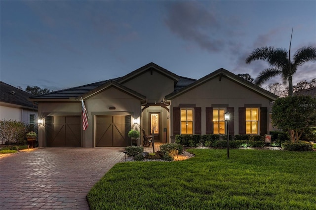 ranch-style house featuring a garage, stucco siding, decorative driveway, and a yard