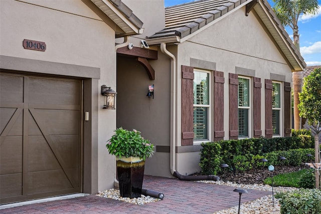 view of exterior entry with a garage, a tiled roof, and stucco siding