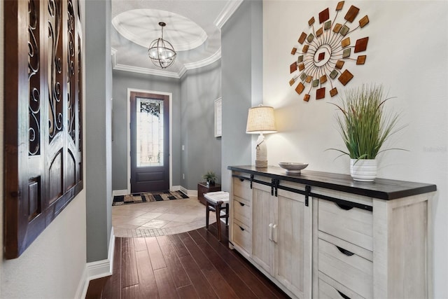 entryway with baseboards, a raised ceiling, ornamental molding, dark wood-type flooring, and a notable chandelier