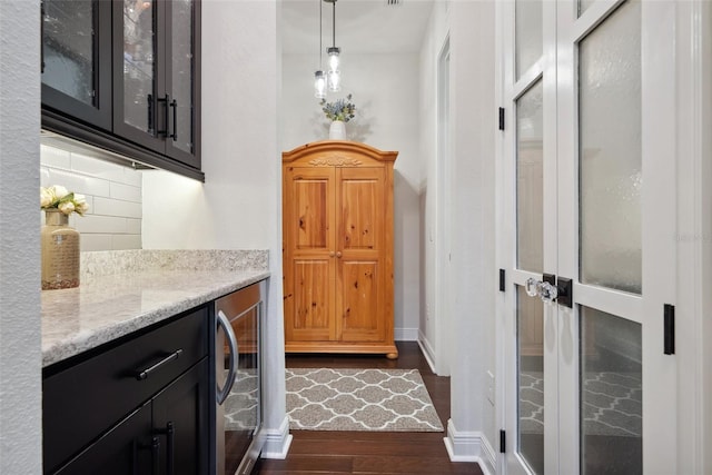 interior space featuring light stone counters, beverage cooler, dark wood-style flooring, decorative backsplash, and glass insert cabinets