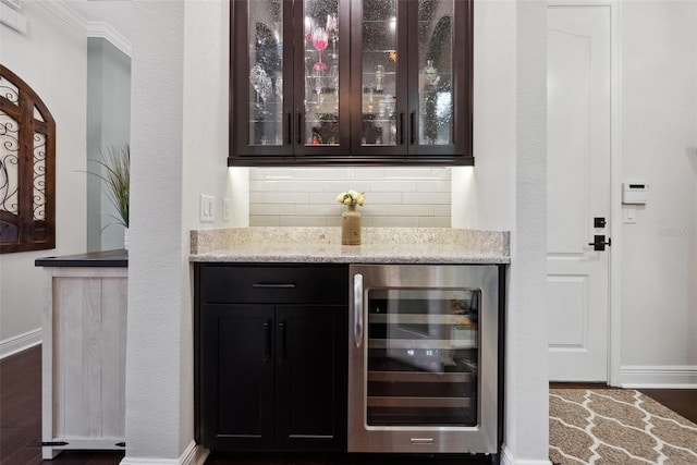 bar with beverage cooler, baseboards, decorative backsplash, dark wood finished floors, and a bar