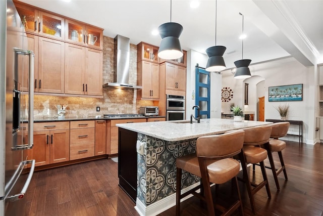 kitchen featuring dark wood-style floors, tasteful backsplash, appliances with stainless steel finishes, light stone countertops, and wall chimney exhaust hood