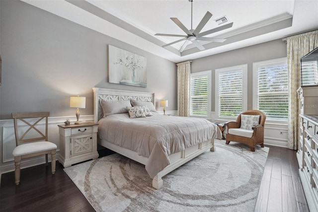 bedroom with a tray ceiling, visible vents, ornamental molding, wainscoting, and hardwood / wood-style flooring