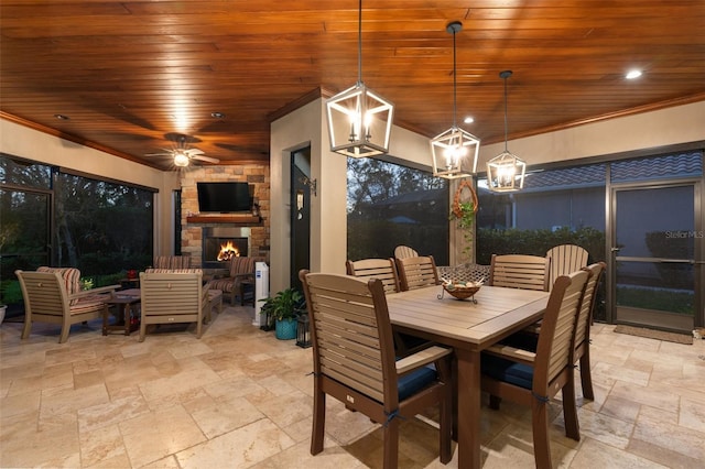 dining area featuring wood ceiling, an outdoor stone fireplace, stone tile floors, and crown molding