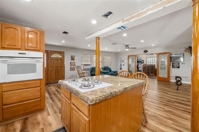 kitchen featuring a center island, light wood-type flooring, decorative columns, white appliances, and a ceiling fan