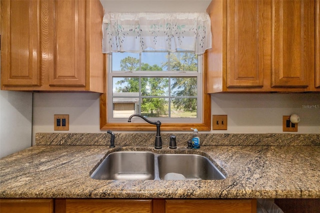 kitchen with brown cabinetry, dark stone countertops, and a sink