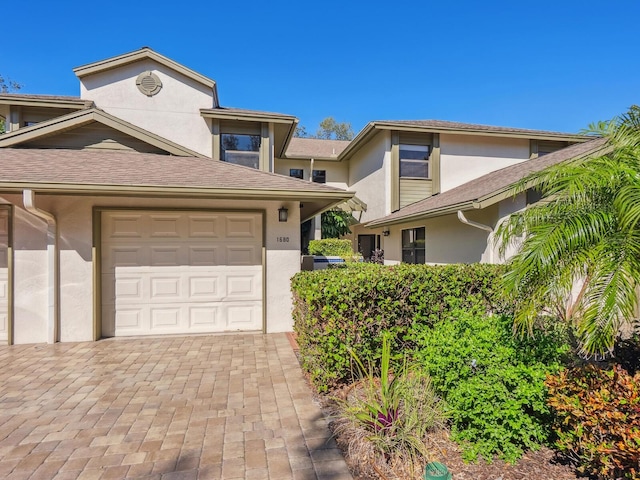 view of front of property with stucco siding, a shingled roof, and decorative driveway