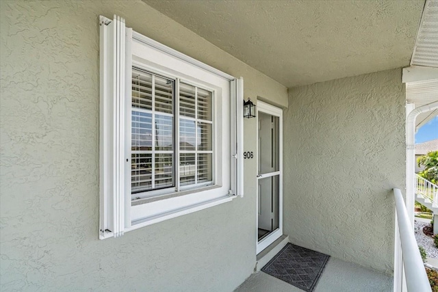 view of exterior entry with a balcony and stucco siding