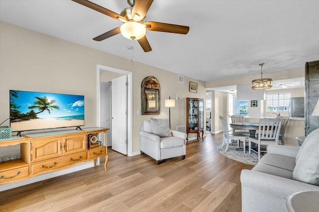 living room featuring baseboards, light wood finished floors, visible vents, and a ceiling fan