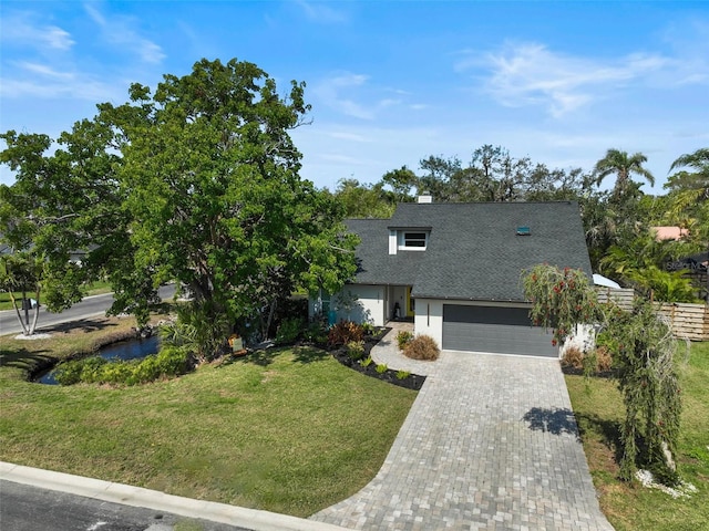 view of front of house featuring a shingled roof, decorative driveway, and a front lawn