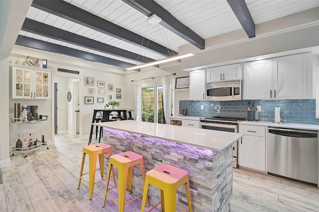 kitchen featuring tasteful backsplash, stainless steel appliances, light wood-type flooring, a kitchen bar, and white cabinetry