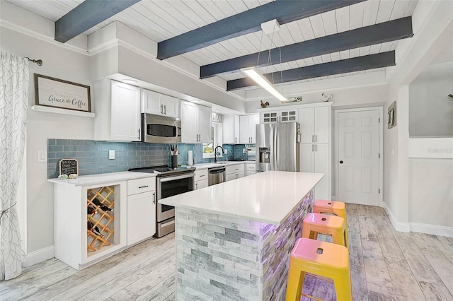 kitchen featuring a breakfast bar area, a sink, light countertops, appliances with stainless steel finishes, and backsplash