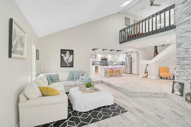 living room with high vaulted ceiling, a ceiling fan, stairs, beam ceiling, and light wood finished floors