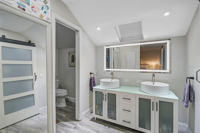 bathroom with double vanity, vaulted ceiling, a sink, and wood finished floors