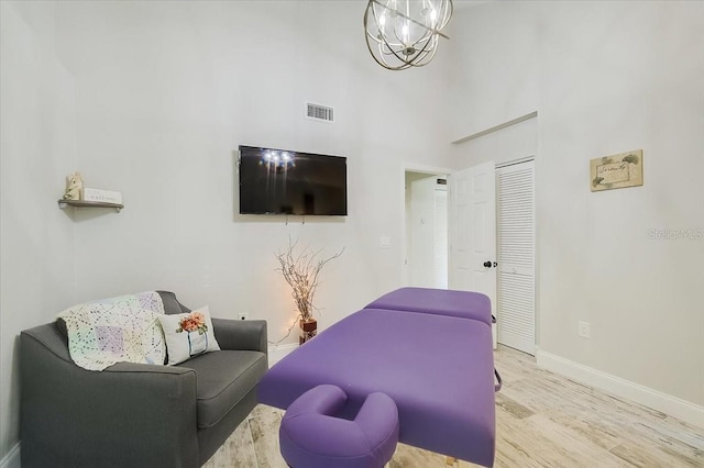 living area with visible vents, a towering ceiling, wood finished floors, a chandelier, and baseboards