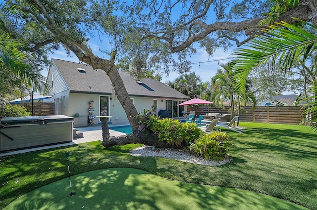 rear view of property featuring a patio, stucco siding, a lawn, a hot tub, and a fenced backyard