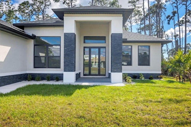 exterior space with a shingled roof, a yard, french doors, stone siding, and stucco siding