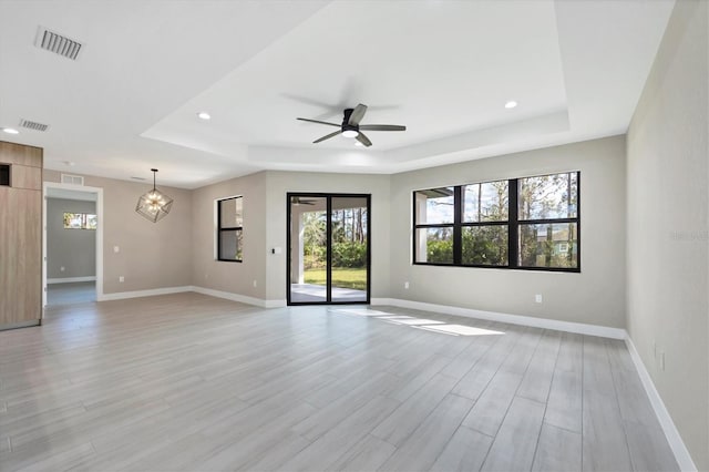 spare room with visible vents, a tray ceiling, baseboards, and ceiling fan with notable chandelier