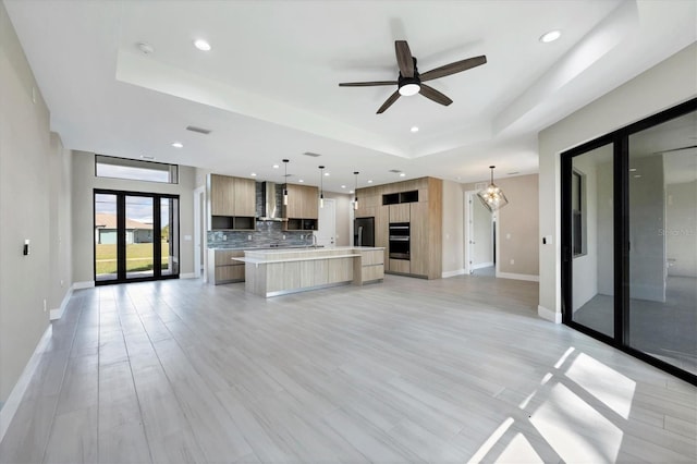 kitchen featuring a raised ceiling, modern cabinets, open floor plan, a center island, and light countertops