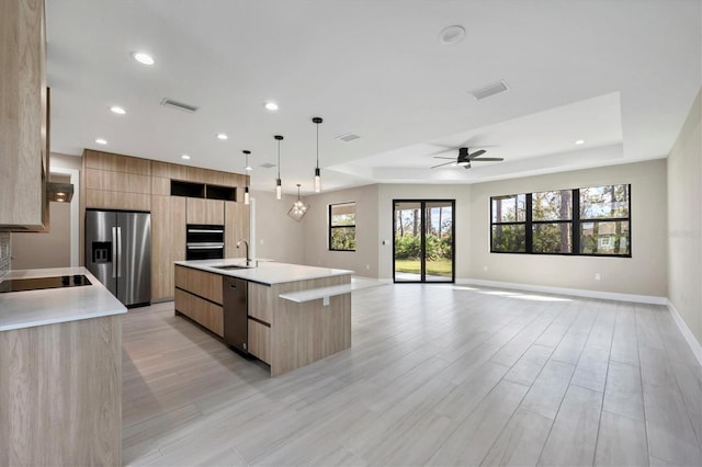 kitchen featuring a center island with sink, modern cabinets, decorative light fixtures, stainless steel appliances, and light countertops