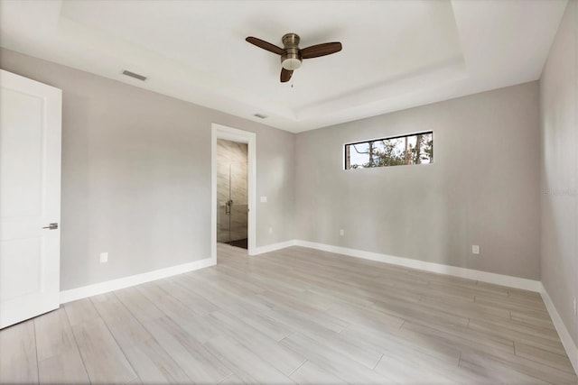 empty room featuring ceiling fan, visible vents, baseboards, light wood-style floors, and a tray ceiling