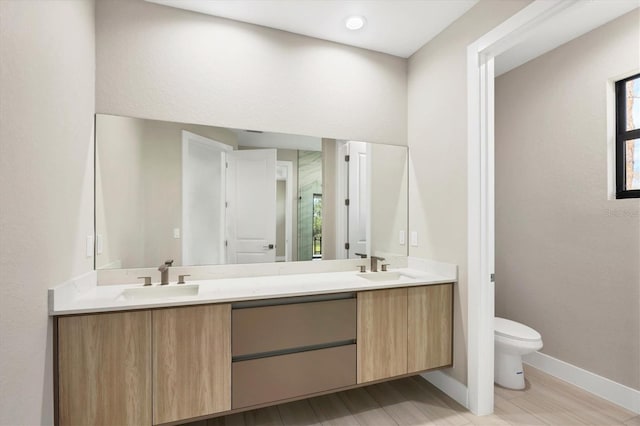 full bathroom featuring double vanity, toilet, a stall shower, a sink, and baseboards