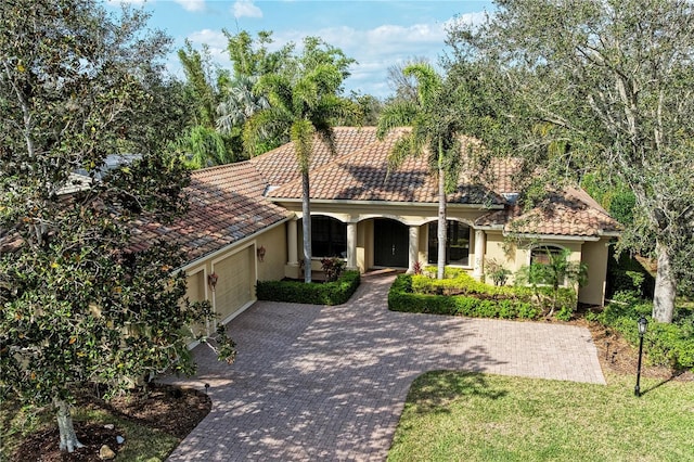 mediterranean / spanish-style home featuring a garage, a tile roof, decorative driveway, and stucco siding