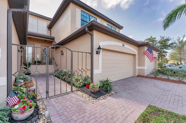 view of home's exterior featuring decorative driveway, an attached garage, a gate, and stucco siding