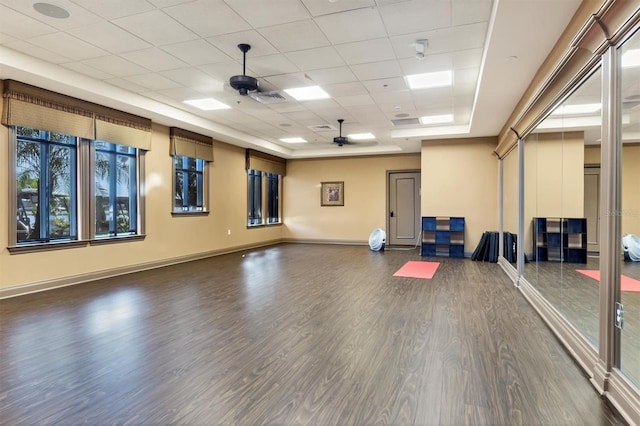 exercise room featuring a paneled ceiling, a ceiling fan, baseboards, dark wood-style floors, and a raised ceiling