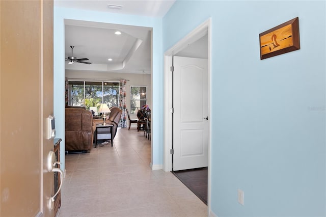 hall featuring a tray ceiling and light tile patterned floors