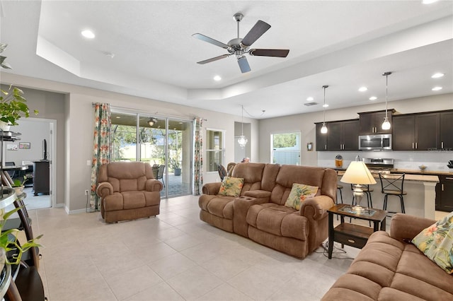 tiled living room with ceiling fan, a raised ceiling, and a wealth of natural light