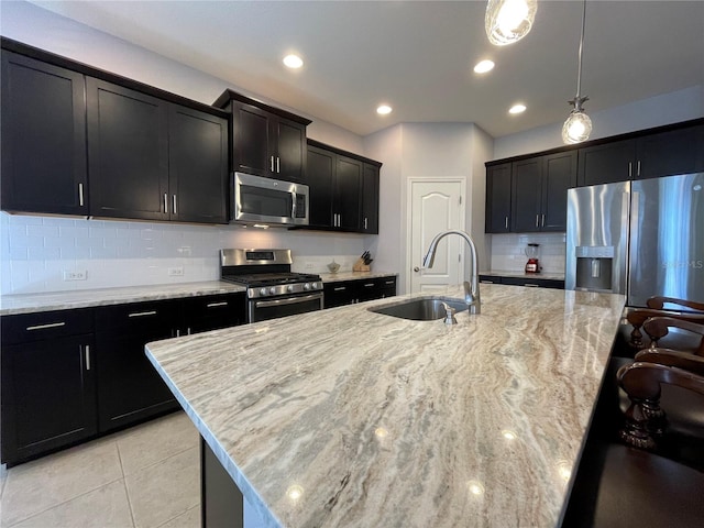 kitchen featuring a center island with sink, appliances with stainless steel finishes, sink, light stone counters, and decorative light fixtures