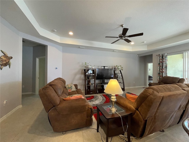 living room featuring a tray ceiling, ceiling fan, and a textured ceiling