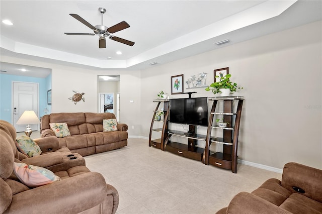 living room featuring light tile patterned flooring, ceiling fan, and a raised ceiling