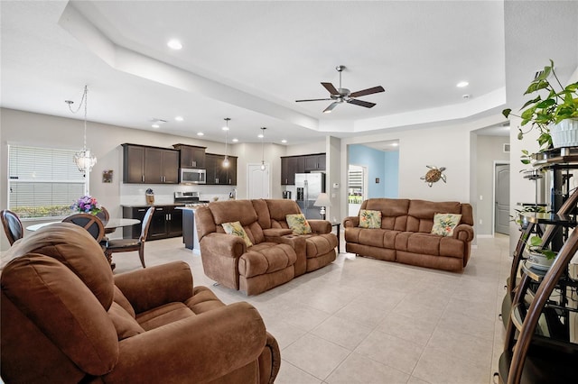 living room featuring ceiling fan with notable chandelier, light tile patterned floors, and a raised ceiling