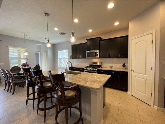 kitchen featuring a center island with sink, hanging light fixtures, a kitchen breakfast bar, stainless steel appliances, and sink