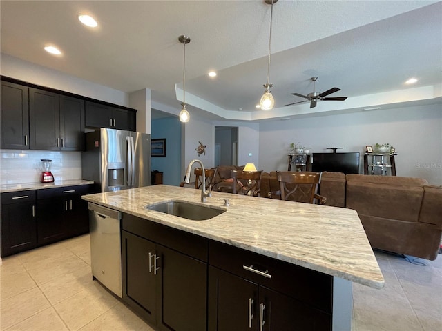 kitchen featuring an island with sink, stainless steel appliances, hanging light fixtures, sink, and a raised ceiling