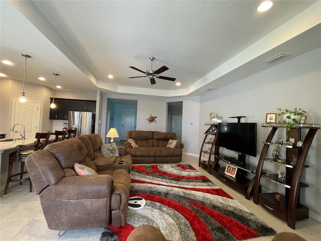 living room featuring ceiling fan, light tile patterned floors, a tray ceiling, and a textured ceiling