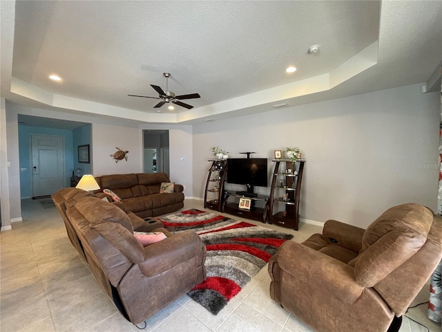 tiled living room featuring a tray ceiling, a textured ceiling, and ceiling fan