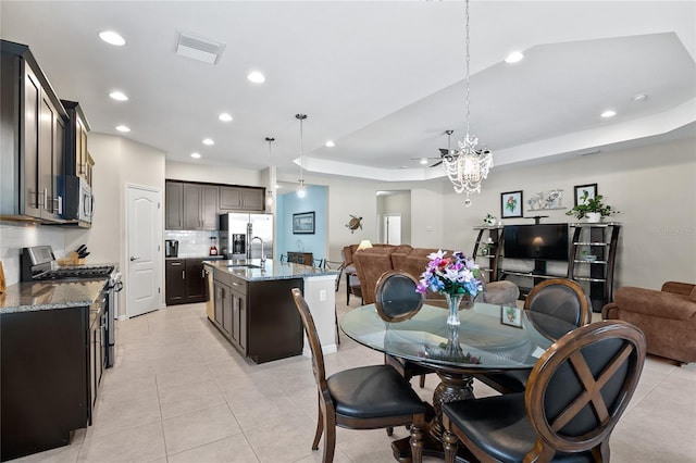 dining space featuring a raised ceiling, sink, light tile patterned flooring, and a notable chandelier