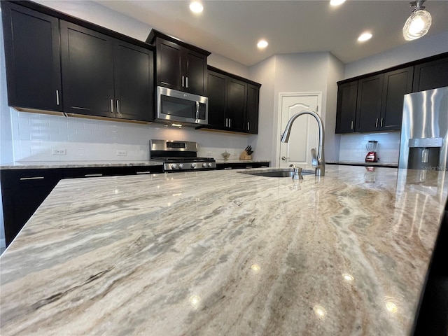 kitchen with sink, light stone counters, stainless steel appliances, hanging light fixtures, and tasteful backsplash