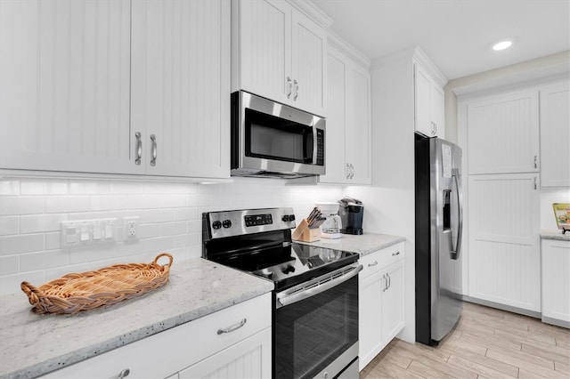 kitchen with stainless steel appliances, white cabinetry, backsplash, light stone countertops, and light wood finished floors